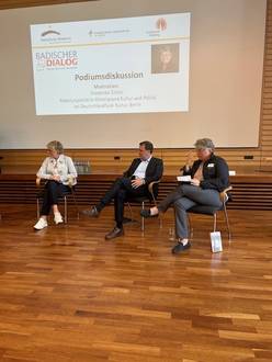 Zwei Frauen und ein Mann sitzen in der Aula und diskutieren.