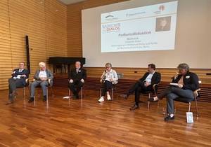 Drei Männer und zwei Frauen sitzen im Halbkreis in der Aula und diskutieren.
